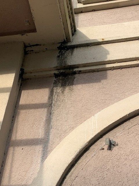 Corner of beige stucco wall with black mildew streaks near the roofline.