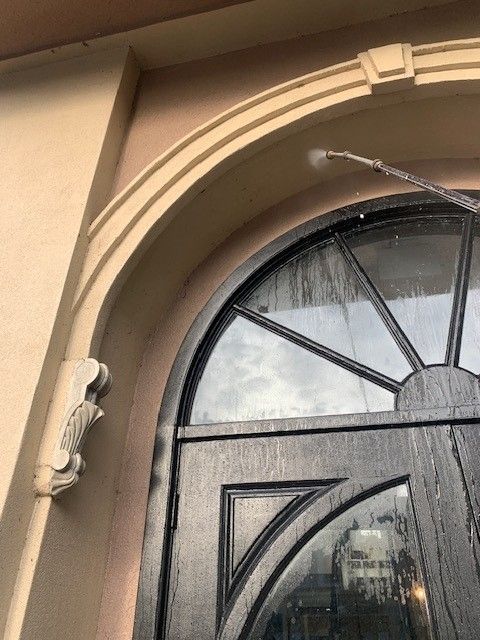 Tan arched doorway with black glass door and water spraying across the top right.