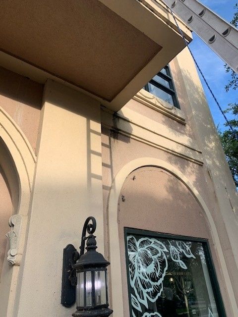 Tan stucco building facade with a black lantern and arched window under a blue sky