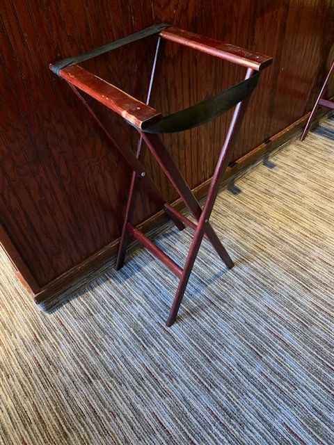 Wooden folding valet stand against a paneled wall on a carpeted floor.