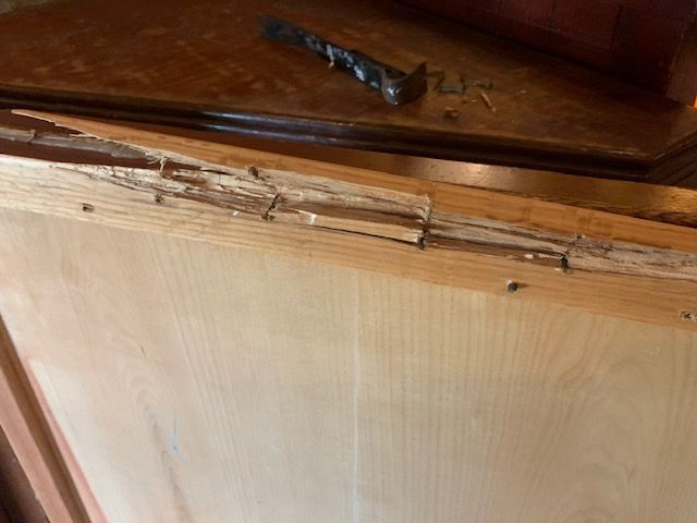 Close-up of a damaged wooden cabinet door with a loose hinge and chipped trim.