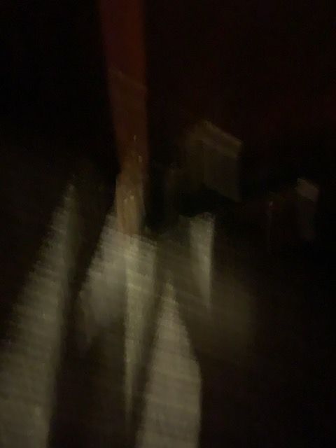 Blurry low-light photo of a person in a striped shirt standing near a wooden post.