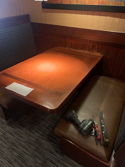Empty restaurant booth with orange table, booth seating, and a drill on a chair
