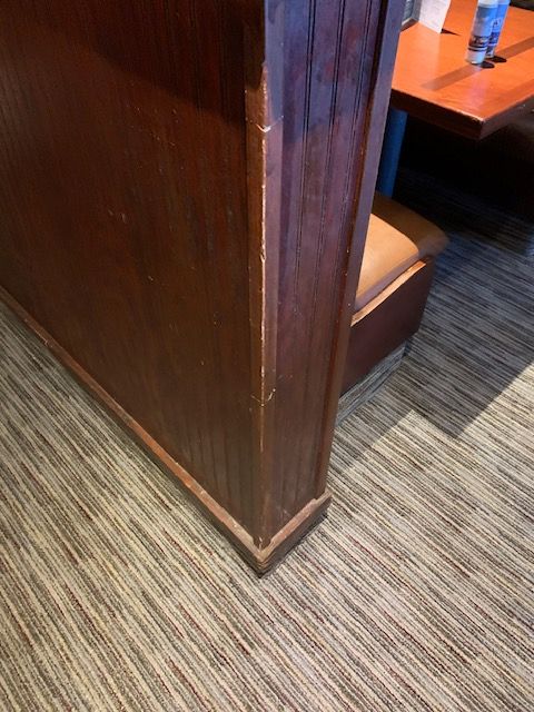 Wooden booth partition beside an orange table in a carpeted restaurant.