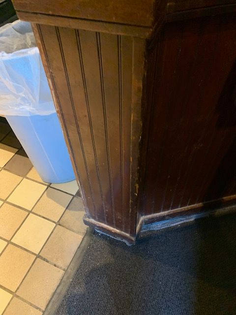Wood-paneled counter corner beside a blue trash bin on a tiled floor