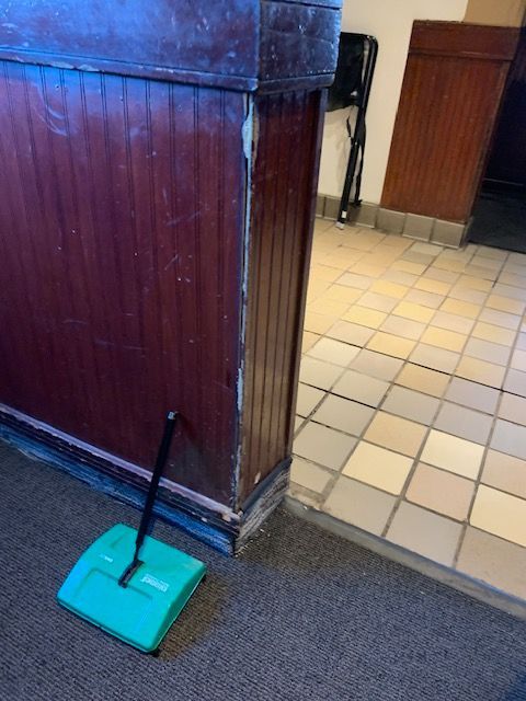 Turquoise dustpan with handle on carpet beside a wooden partition and tiled floor