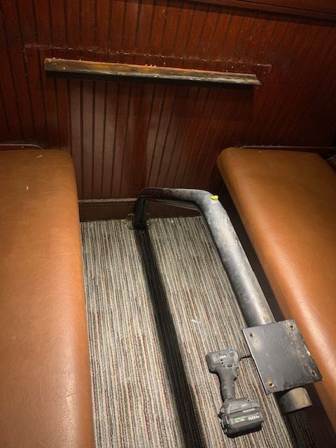 Folded step stool on striped carpet between brown vinyl seats in a wooden interior.