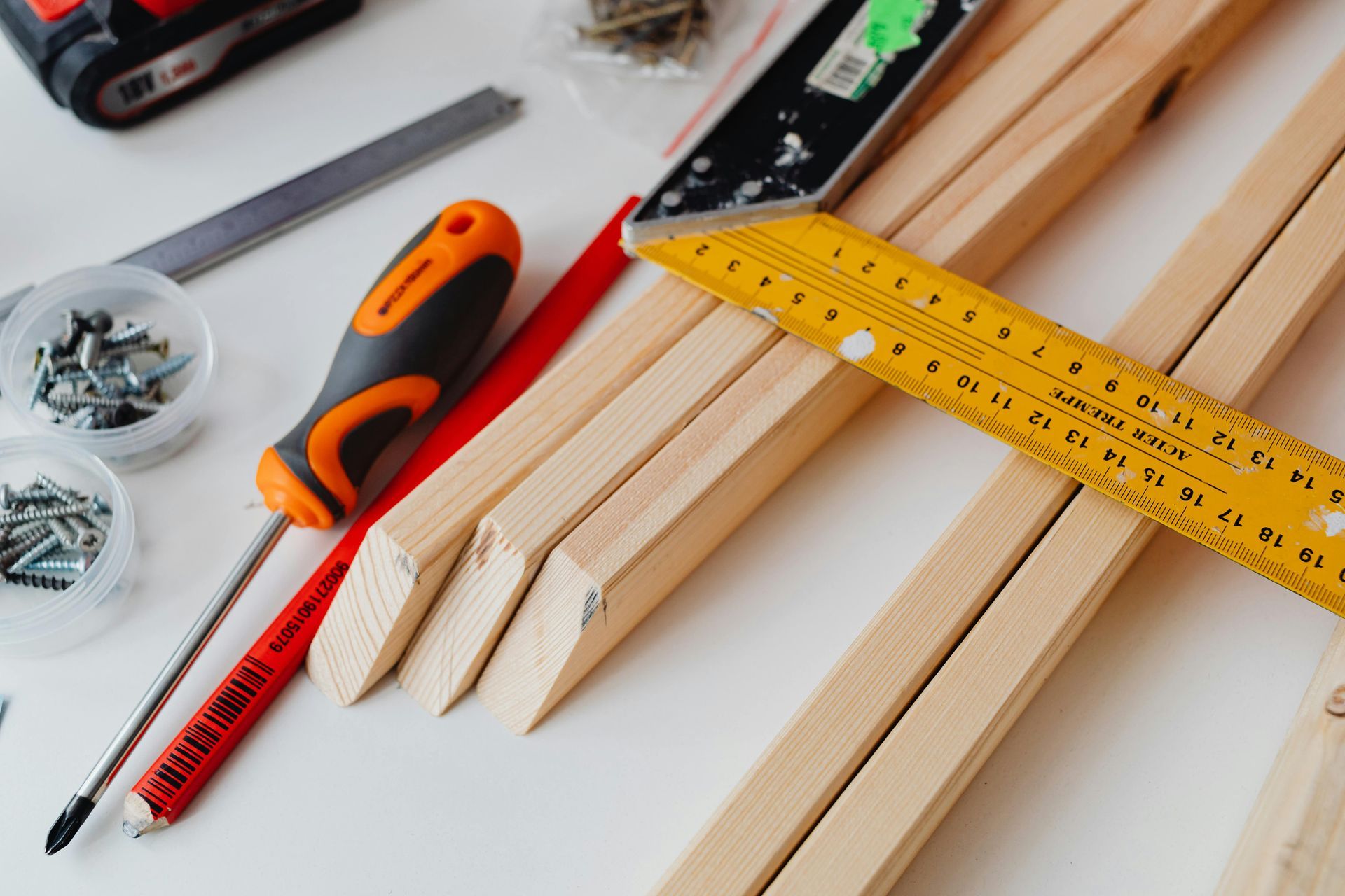 A screwdriver , ruler , and screws are on a wooden table.