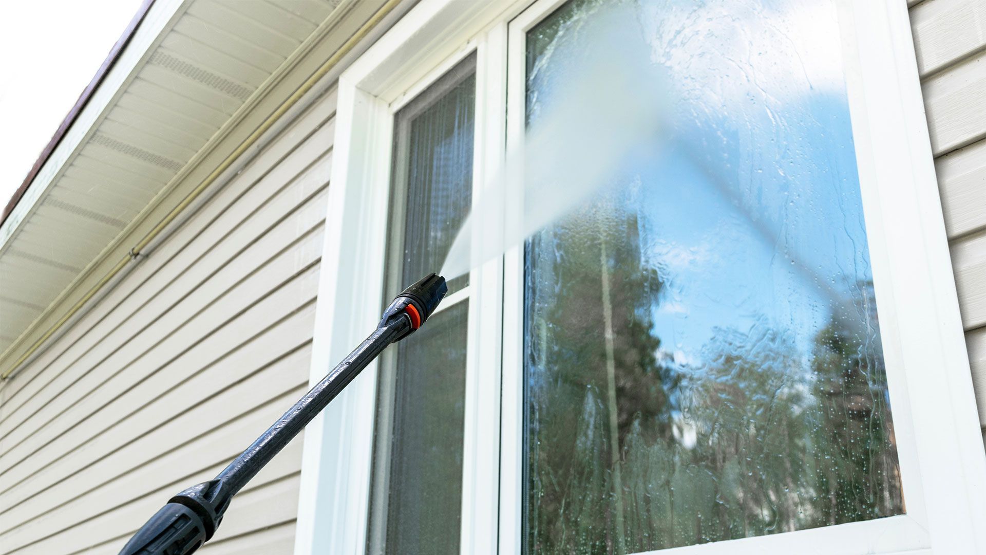 A person is cleaning a window with a high pressure washer.
