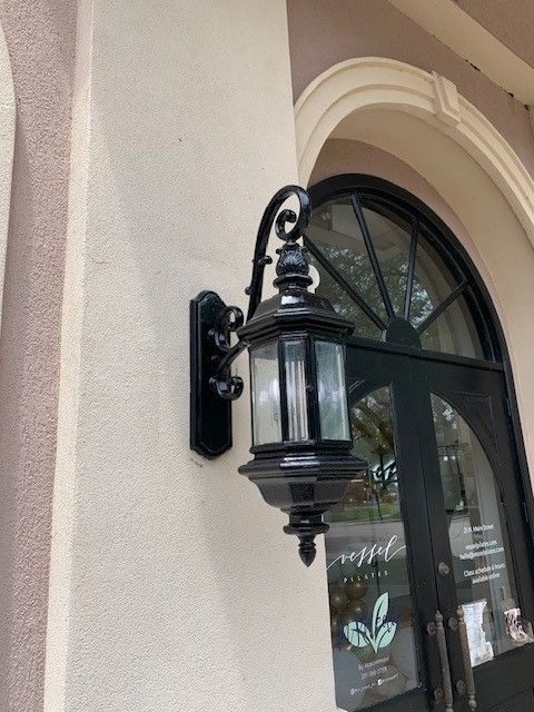 Black outdoor wall lantern mounted beside an arched doorway on a beige stucco wall.