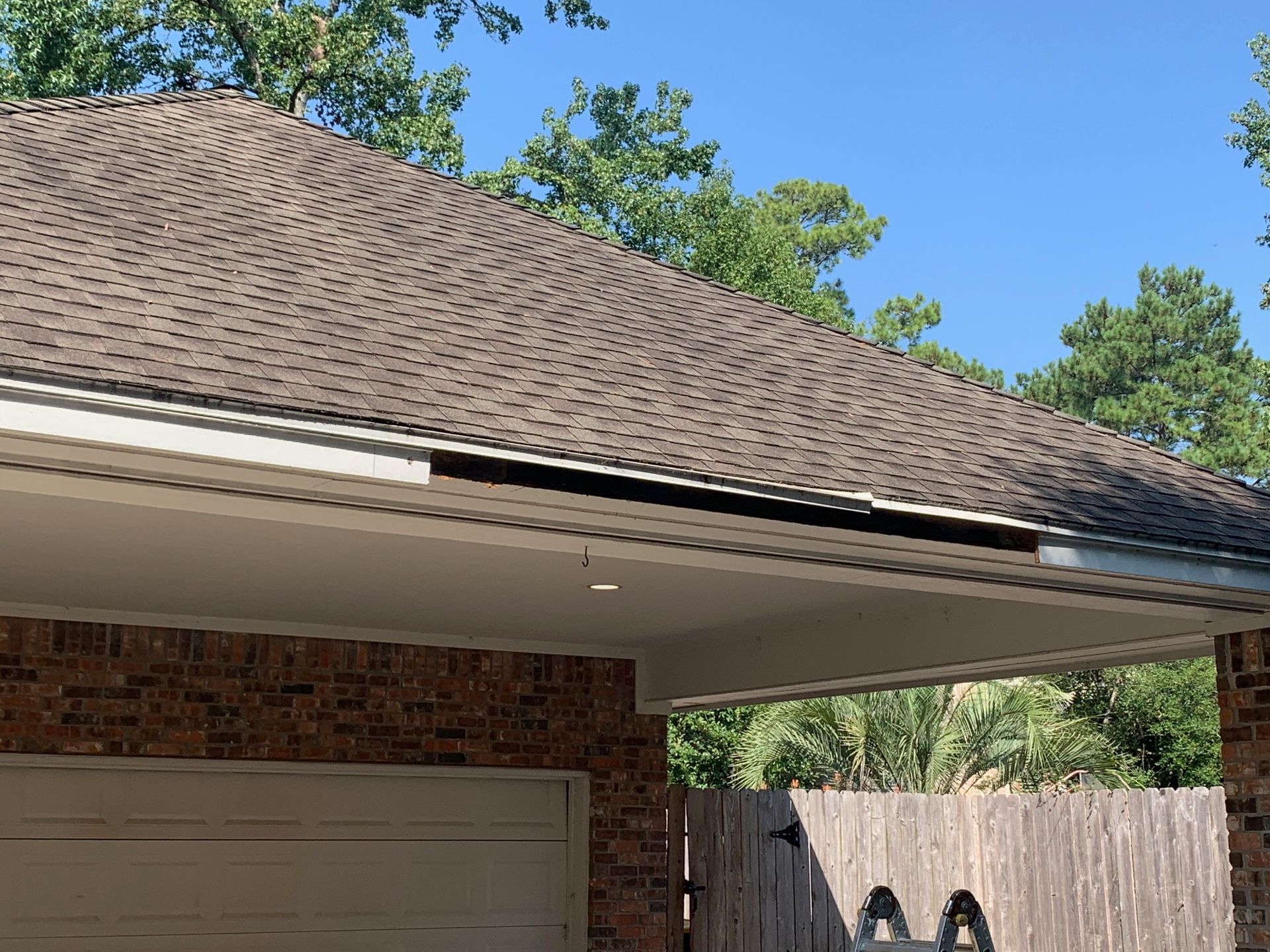 Brick house garage with beige door and shingled roof under a clear blue sky