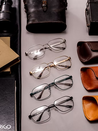 Tres pares de gafas sobre una superficie gris, junto a estuches de cuero en color negro, marrón y tostado.