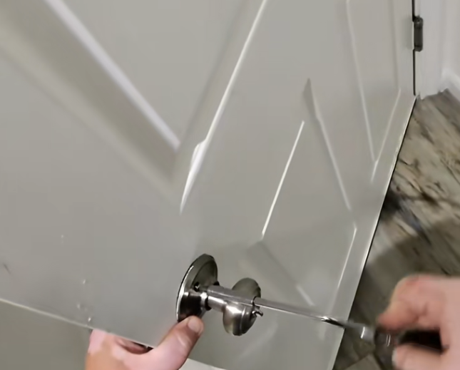 Hand turning a screwdriver to install a silver doorknob on a white door