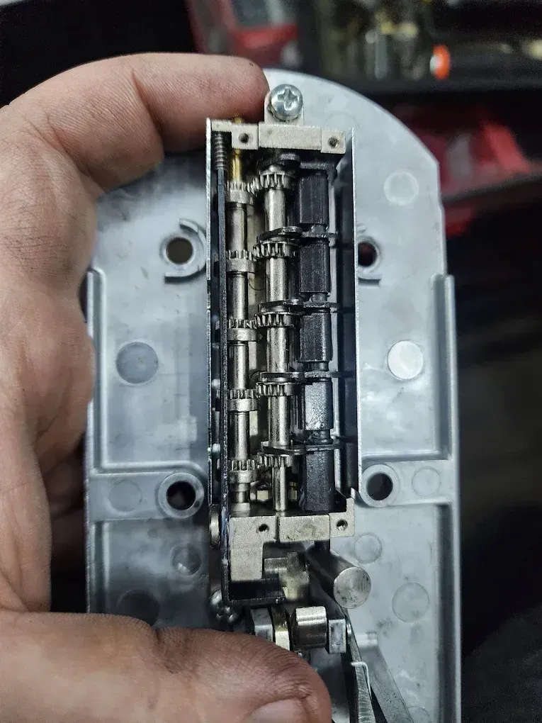 Close-up of a hand holding a small metallic mechanical device with exposed internal parts.