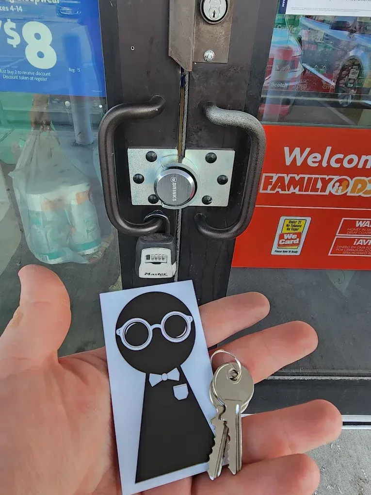 Hand holding a black key tag with a white glasses-and-bowtie face in front of a store door lock