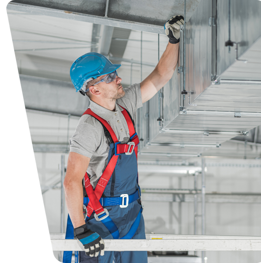 Contact Us Construction worker in blue hard hat and safety harness inspecting overhead ductwork on a scaffold