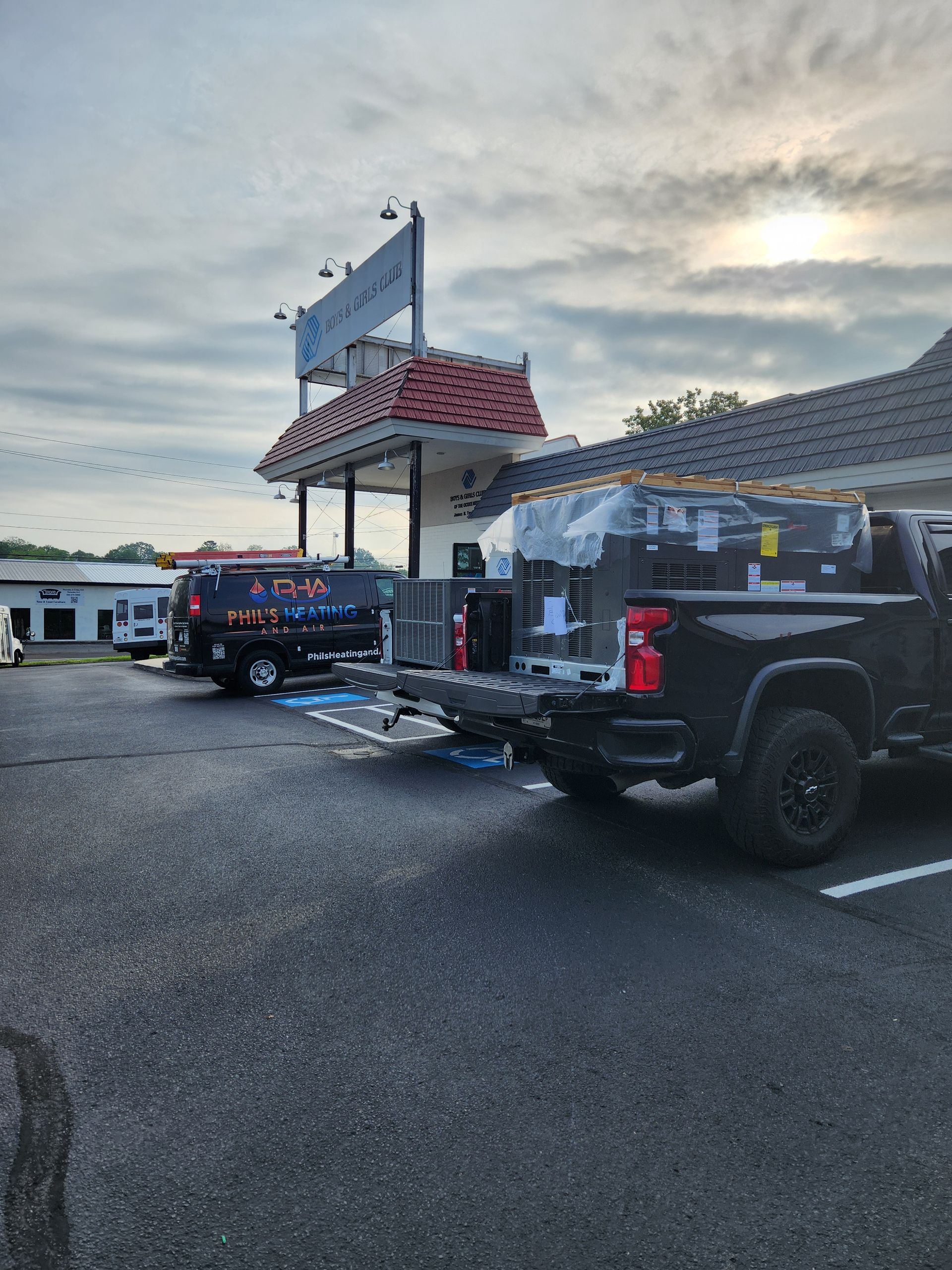 Parked pickup trucks with trailers in a gravel lot beside a building at dusk
