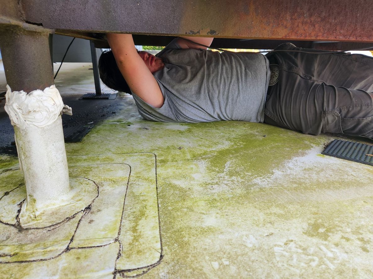 Person lying under a vehicle, reaching up to work underneath on a concrete surface.