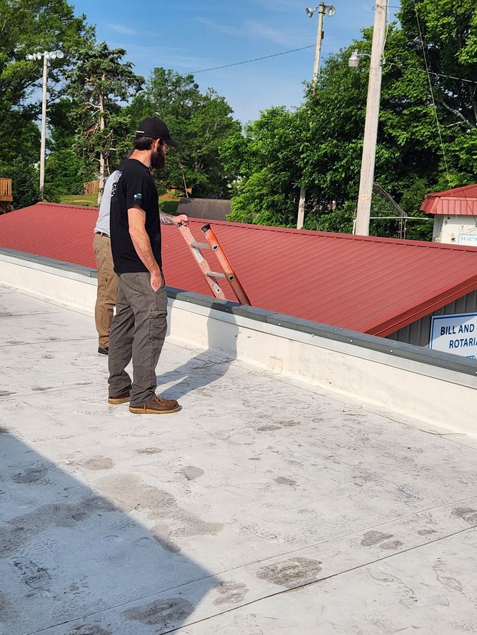 Person standing on a white rooftop beside a red parapet wall, holding a ladder under a blue sky