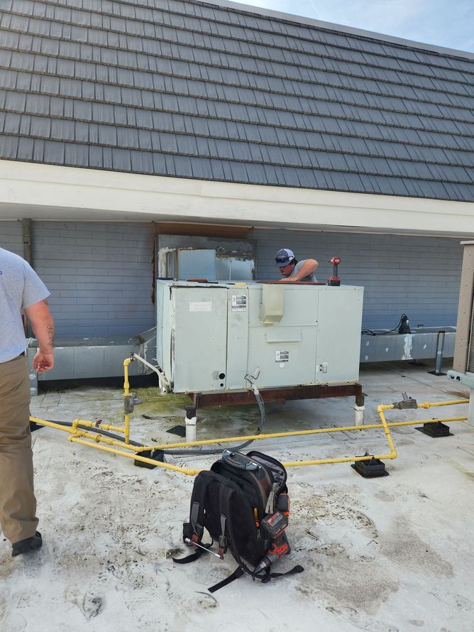 Roof repair workers beside an HVAC unit on a flat roof, with tools and a backpack in the foreground.