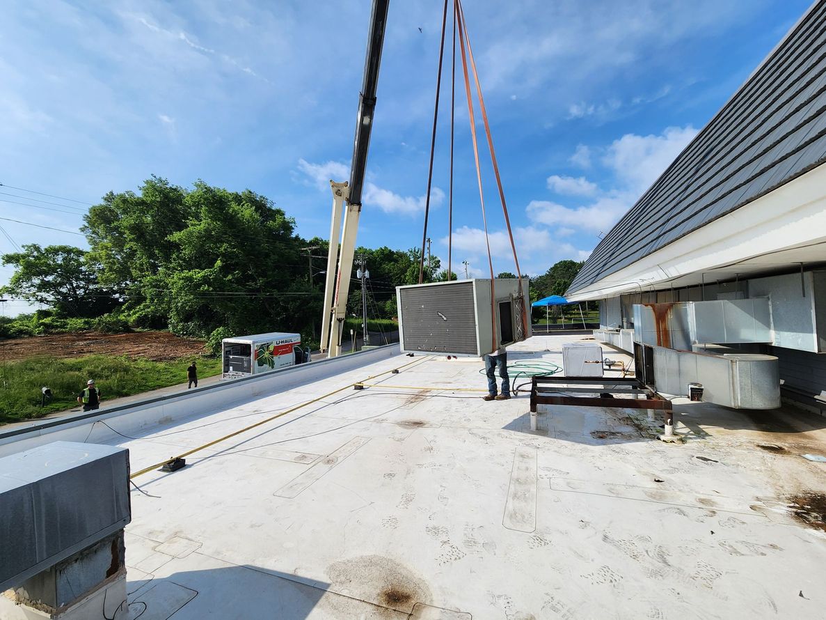 Construction workers lifting a large concrete slab beside a building under construction on a sunny rooftop