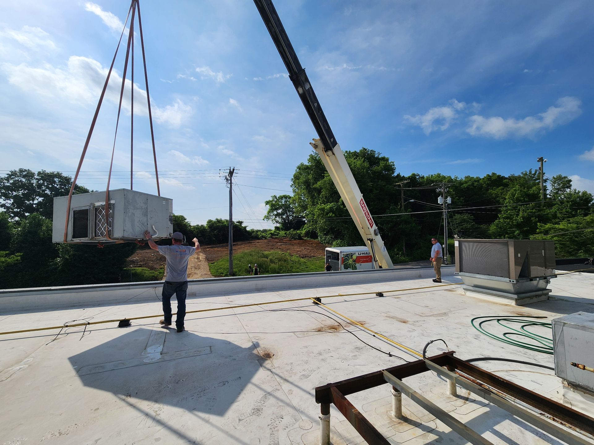 Construction site with crane lifting a white container; workers stand on a concrete slab under a blue sky.