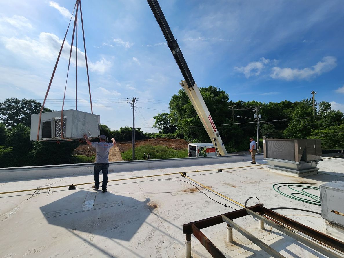 Construction site with crane lifting a white container; workers stand on a concrete slab under a blue sky.