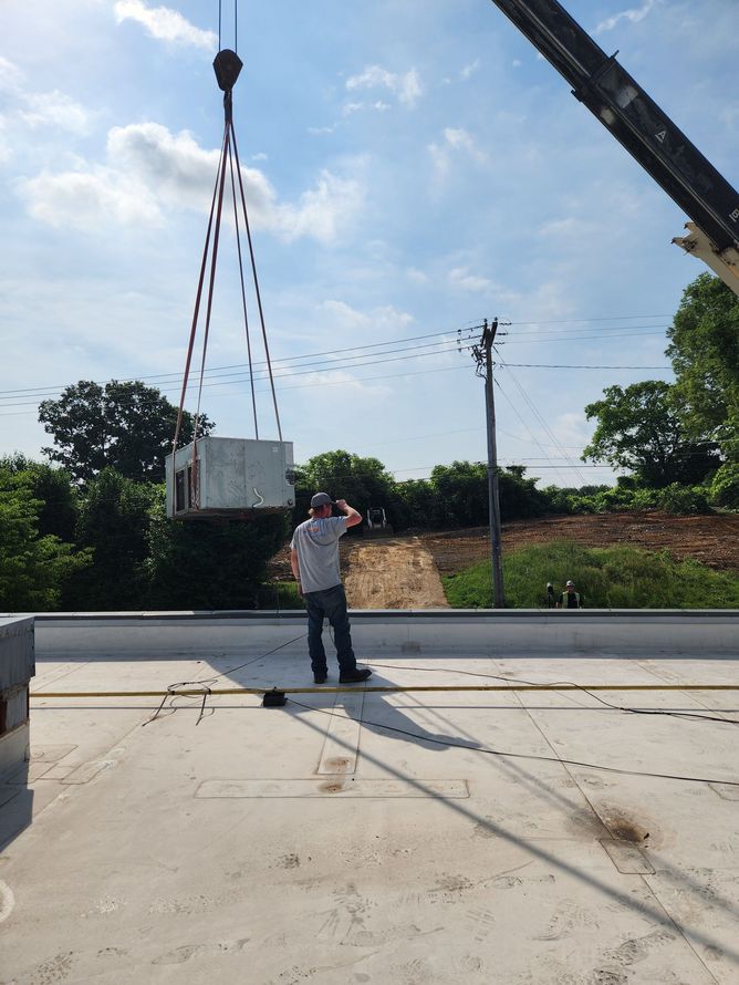 Worker guiding a suspended concrete block at a construction site on a sunny day