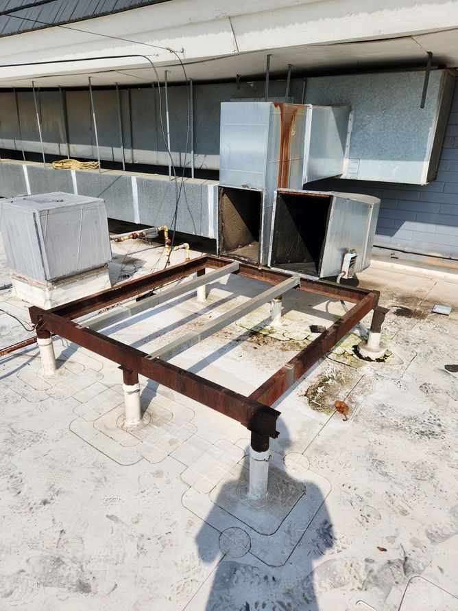 Rooftop with a rusted metal frame, ventilation units, and HVAC equipment under bright sunlight.