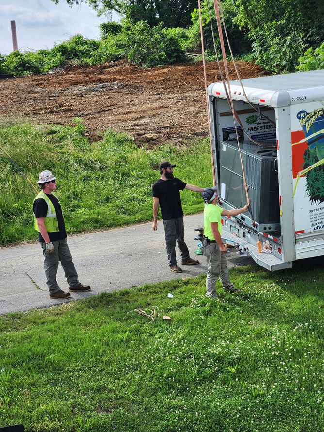 Workers unloading a white truck on a gravel path beside a grassy hill