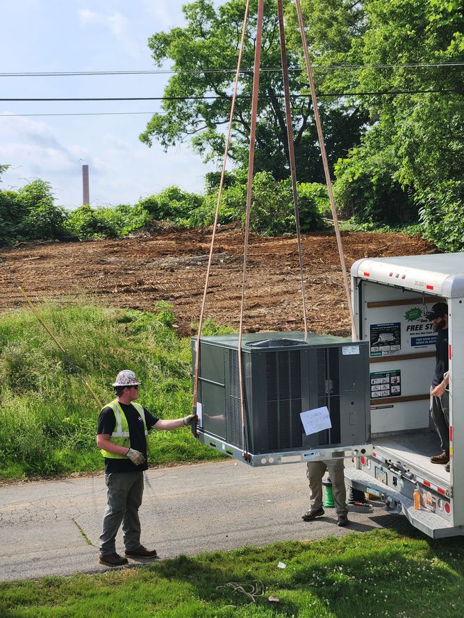 Two workers unloading a large HVAC unit from a truck on a roadside.