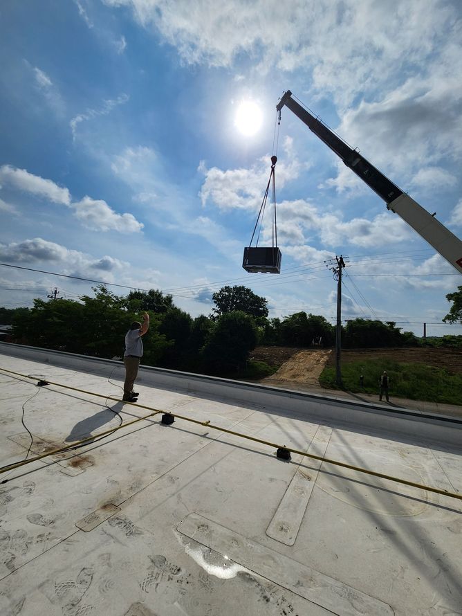 Crane lifting a hanging load over a road under bright sun, with a person standing nearby.