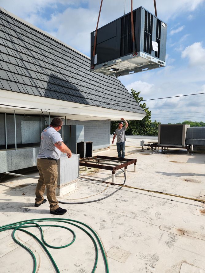 Workers lifting a large HVAC unit by crane onto a rooftop by a white building