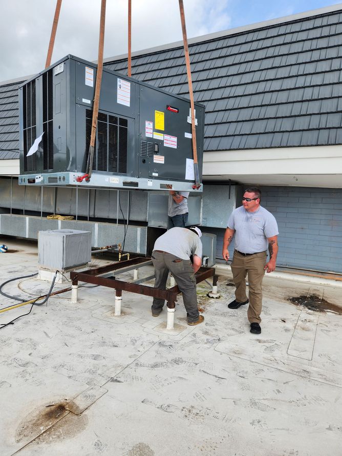 Workers moving a large HVAC unit on a rooftop with crane straps attached