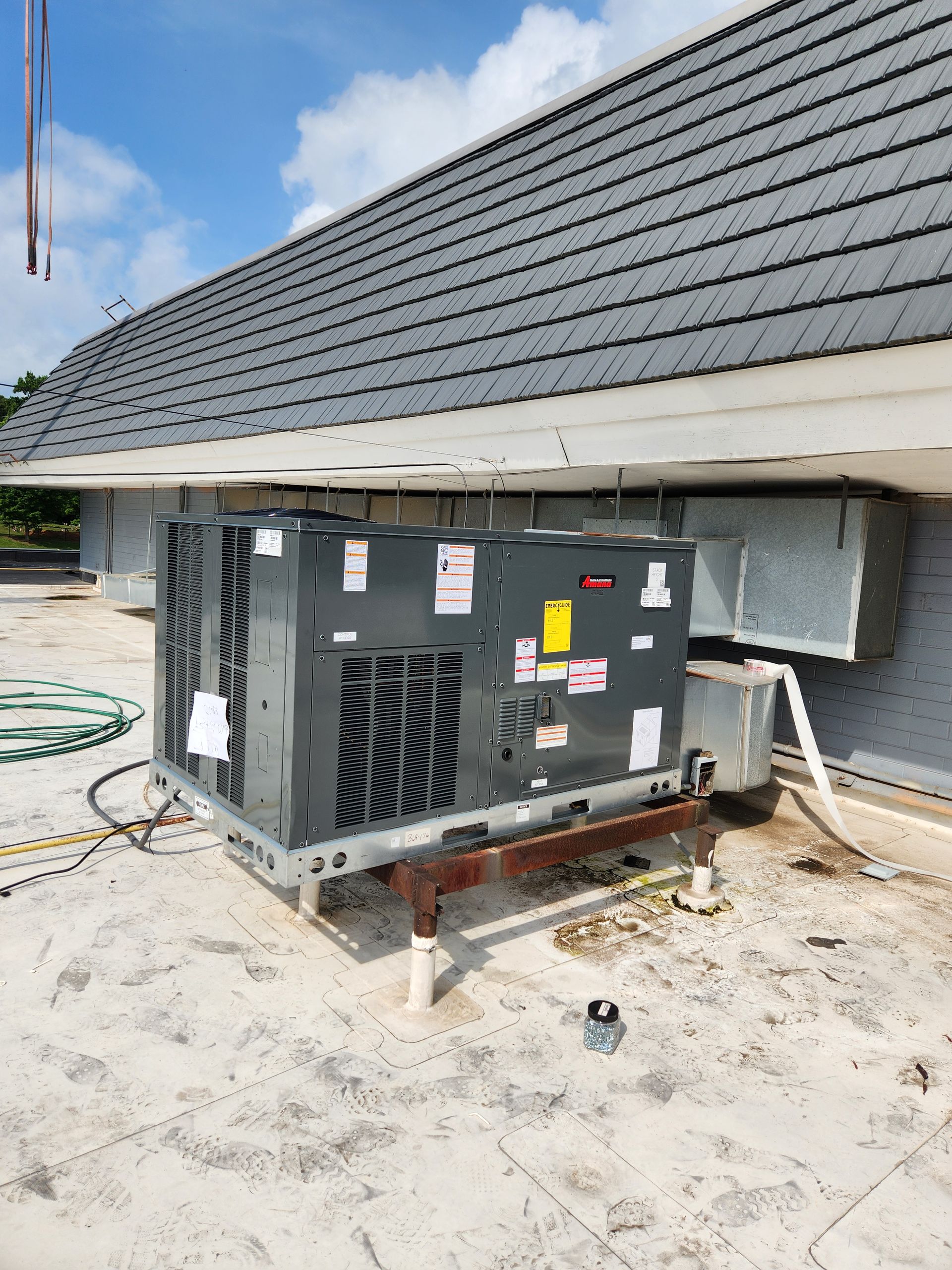 Industrial HVAC unit on a rooftop under a shingled roof, with pipes and wiring visible.