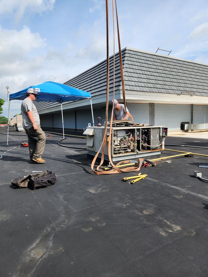 Workers repairing a flat rooftop with a blue canopy and equipment on a black tar roof
