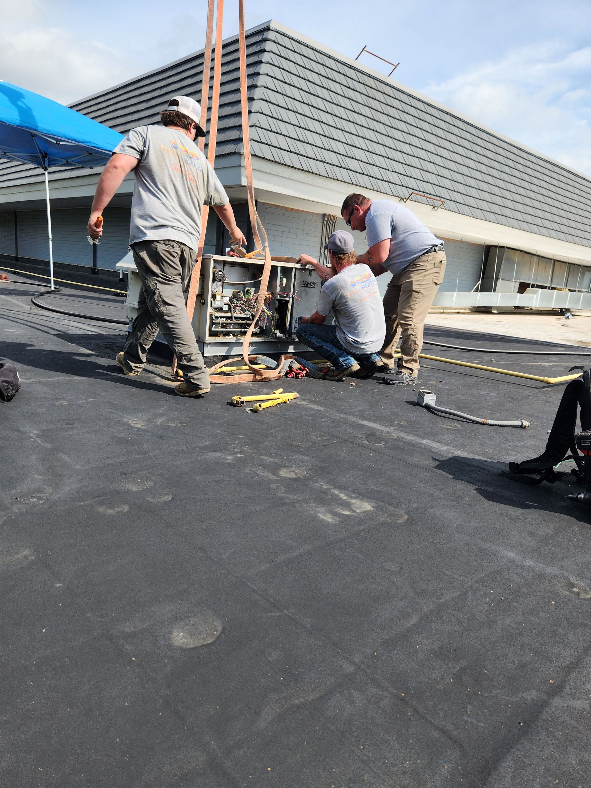 Workers repairing a flat rooftop with tools and equipment under a bright sky.