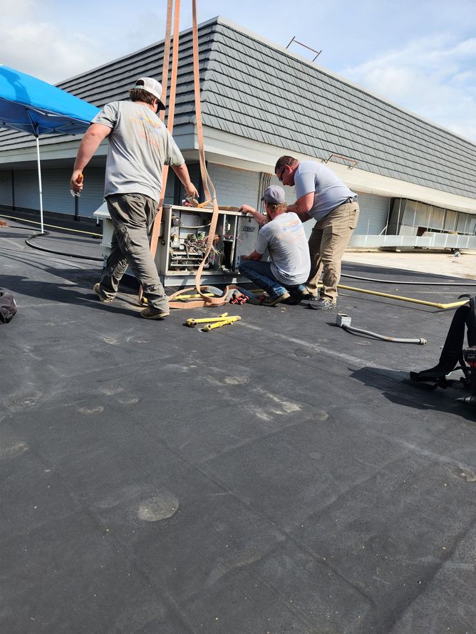 Workers repairing a flat rooftop with tools and equipment under a bright sky.
