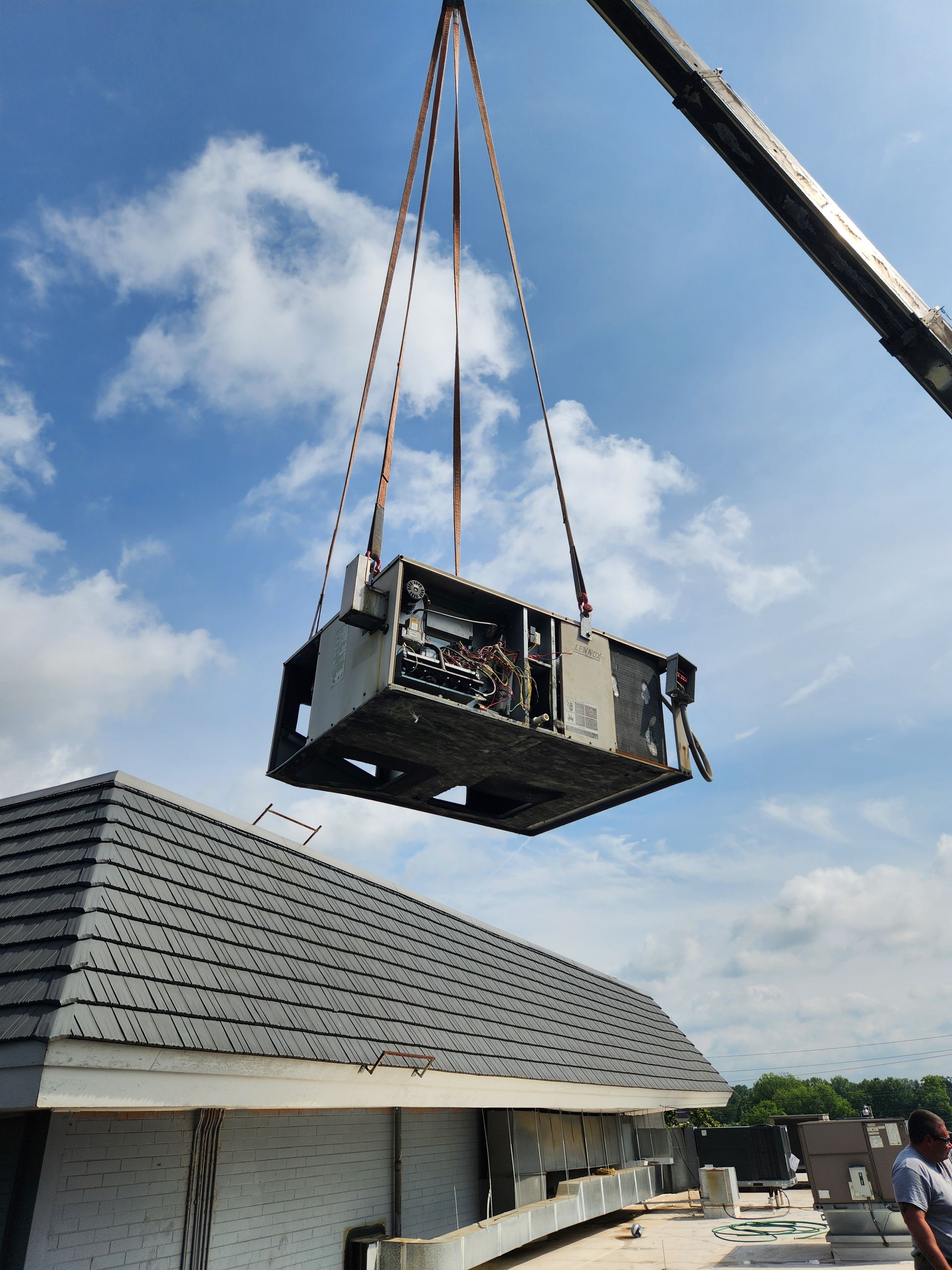 Crane lifting a large unit above a house roof under a blue sky