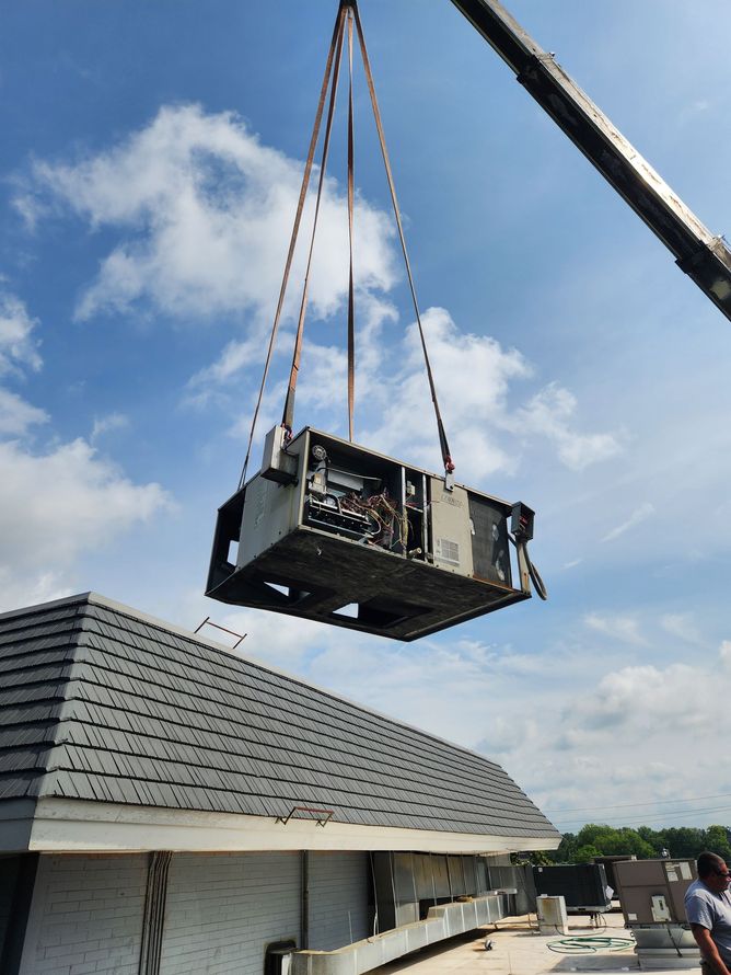 Crane lifting a large unit above a house roof under a blue sky