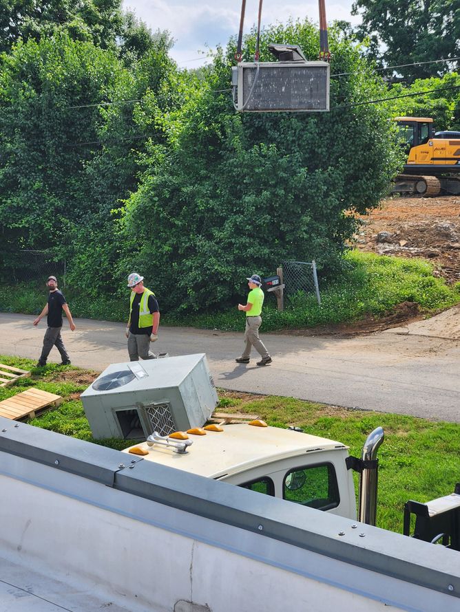 Workers carrying a concrete block across a road near a white truck and construction equipment.