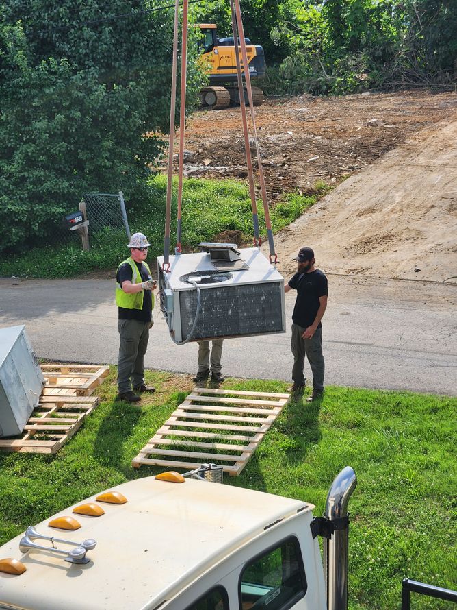 Workers guide a suspended concrete block between ramps in a grassy construction site.