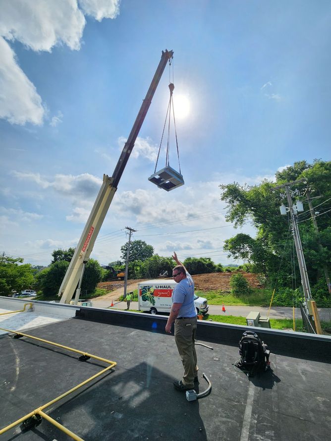 Crane lifting a large platform over a road while a worker watches under a bright blue sky