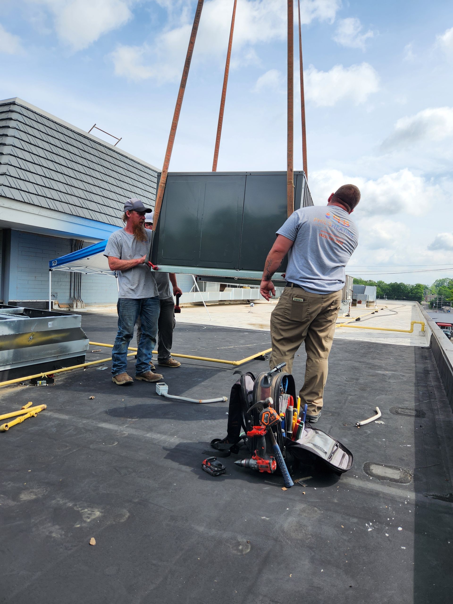 Workers hoisting a large panel onto a rooftop with lifting straps and equipment