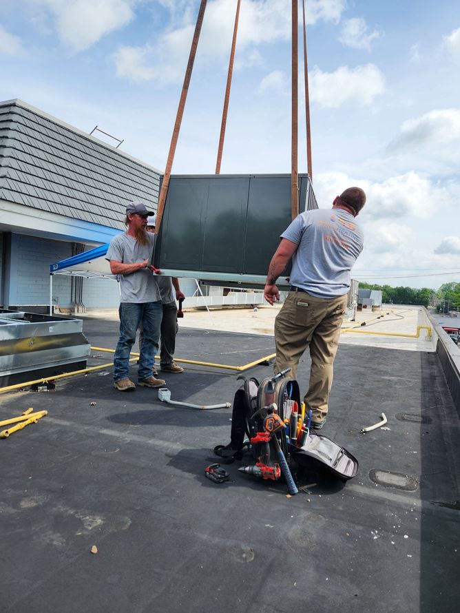 Workers hoisting a large panel onto a rooftop with lifting straps and equipment