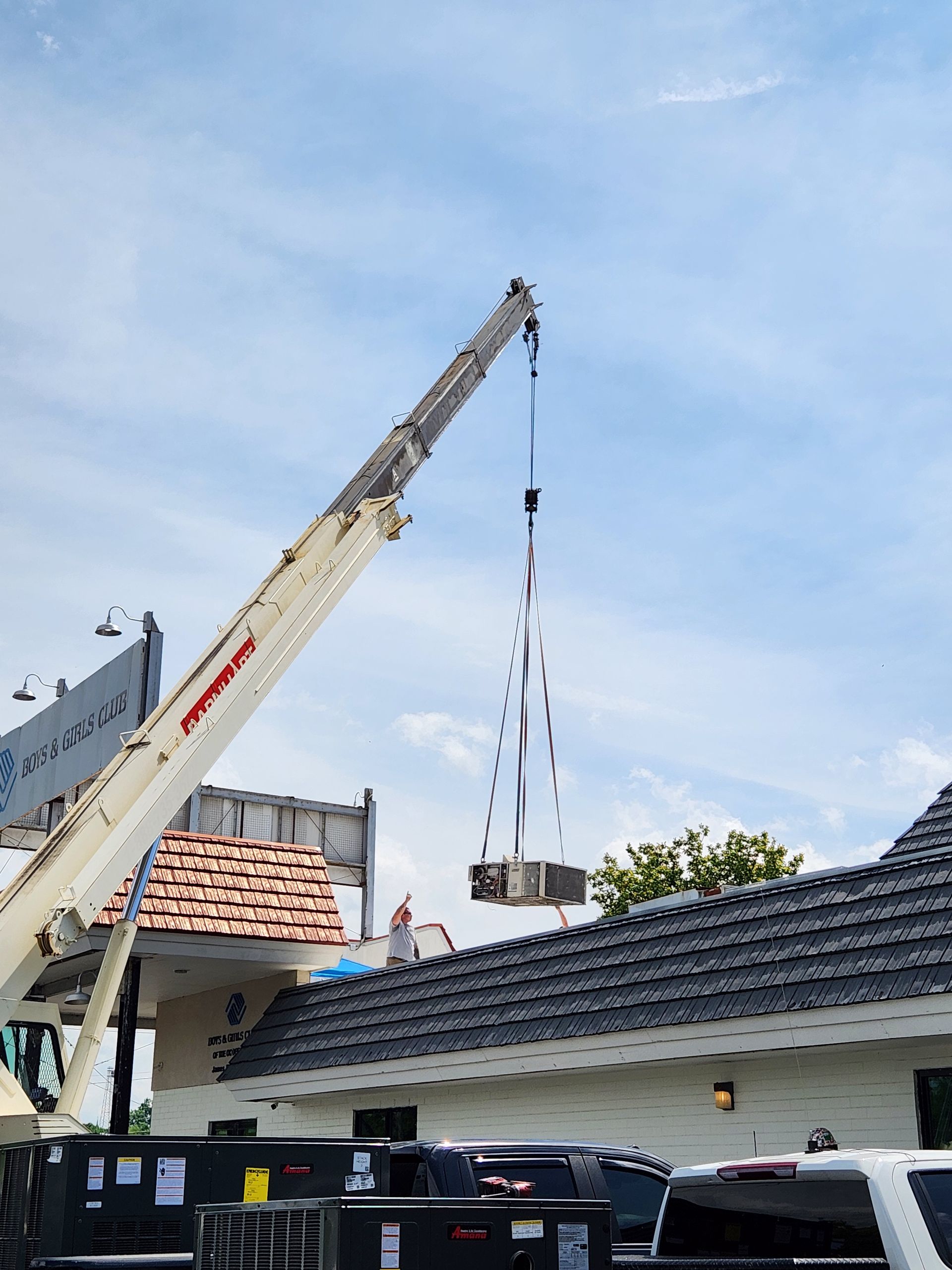 Crane lifting materials over a tiled-roof house under a blue sky