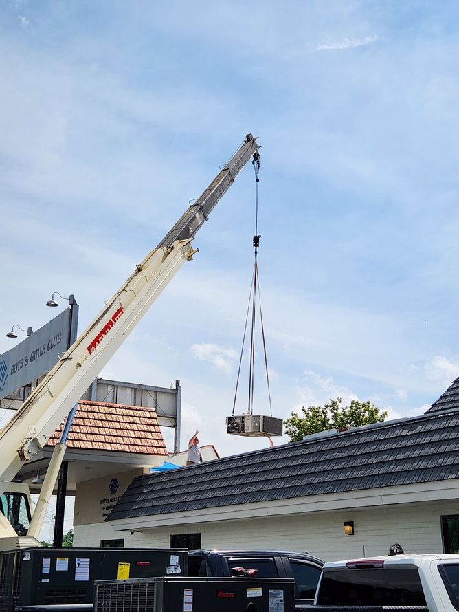 Crane lifting materials over a tiled-roof house under a blue sky