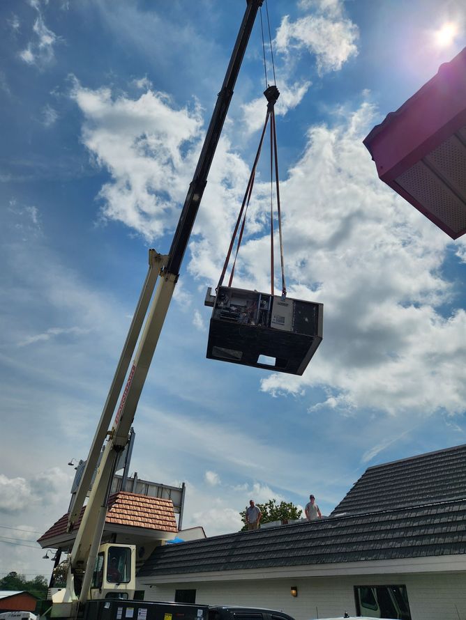 Crane lifting a large black container over a house roof under a bright blue sky