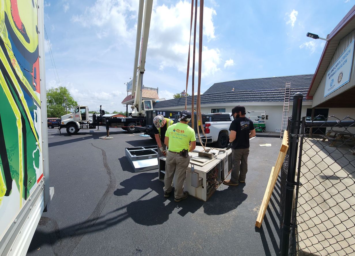 Workers pushing a wheeled bin on a sunny street beside a chain-link fence and parked trucks