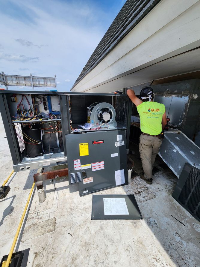 Technician in neon shirt repairing rooftop HVAC unit beside open service panel.